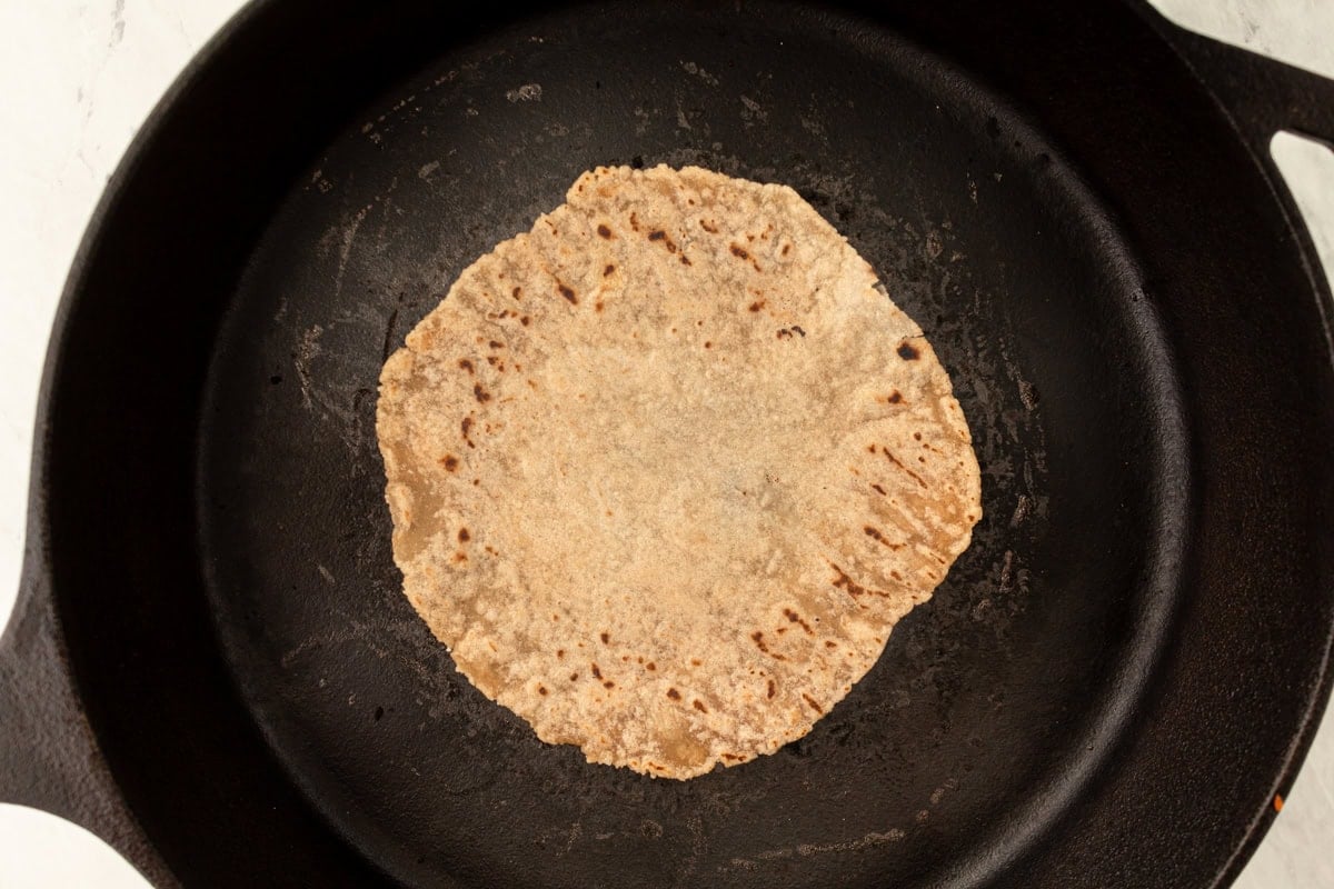 A cassava tortilla cooking in a black cast-iron skillet, showing light browning on the surface.