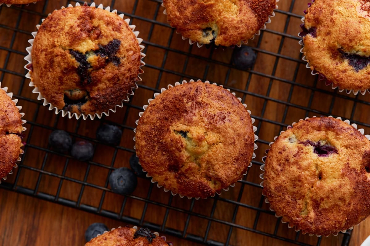 Close-up of freshly baked gluten-free blueberry muffins cooling on a wire rack, with blueberries and a rich, golden top visible.