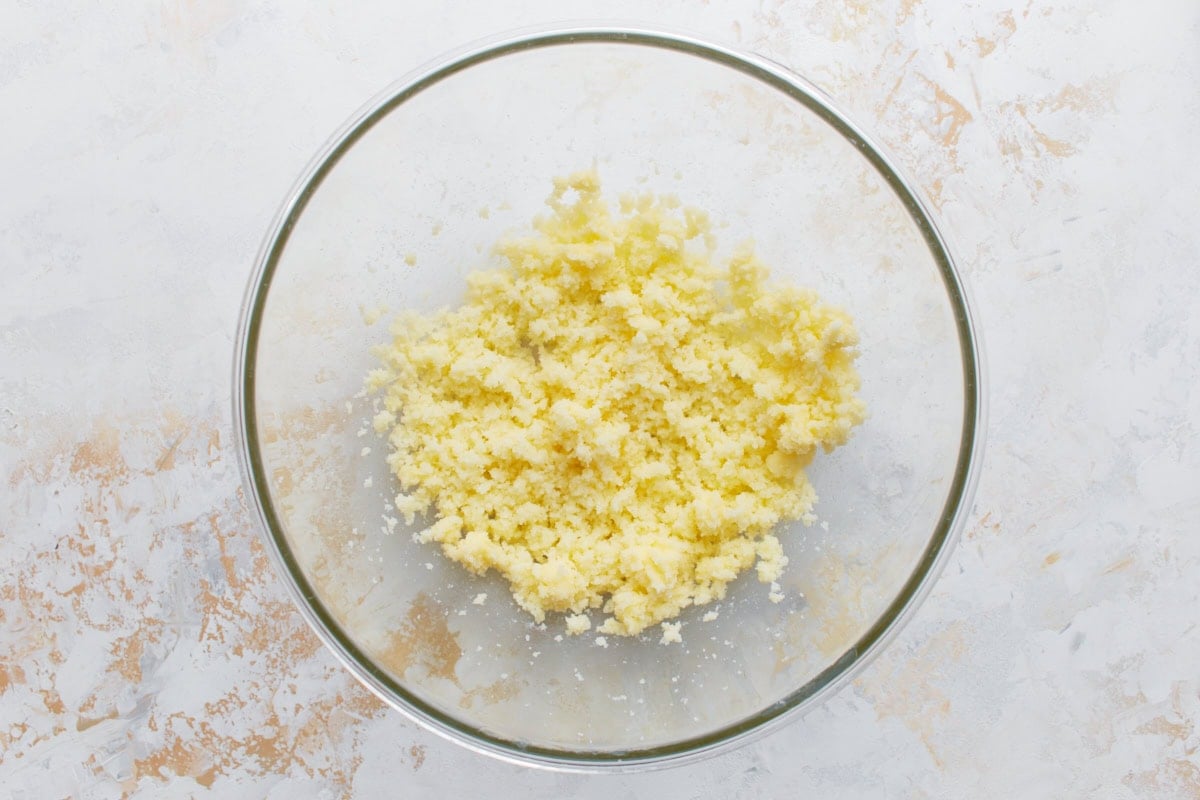Glass mixing bowl with creamed butter and sugar mixture on a white and beige textured surface.