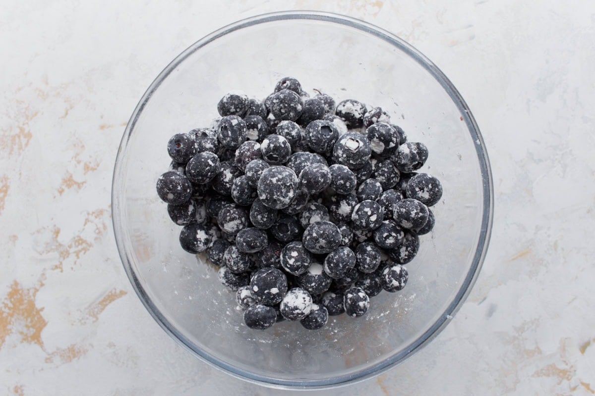 Fresh blueberries coated in flour inside a clear glass bowl, ready to be folded into muffin batter.