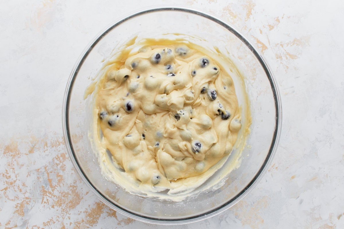 Muffin batter folded with blueberries in a large glass bowl, ready for scooping.