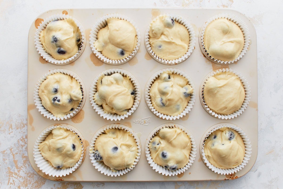 Twelve muffin liners filled with gluten-free blueberry muffin batter in a muffin tin, ready to bake.