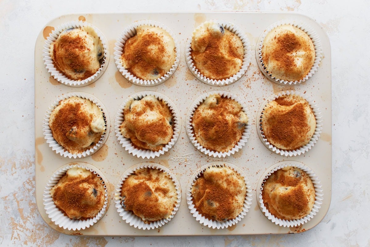 Overhead view of a muffin tin filled with unbaked gluten-free blueberry muffin batter, each topped with a sprinkle of coarse sugar