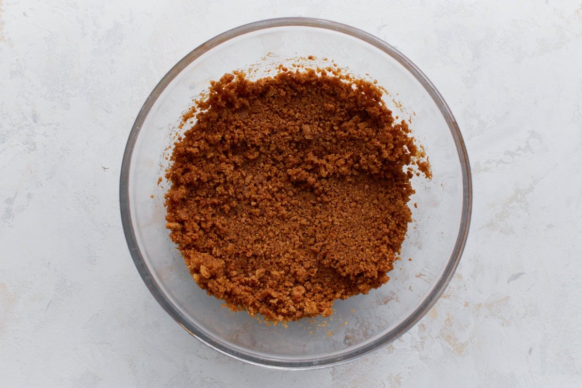 Bowl of crushed gluten-free graham crackers mixed with melted butter for the cheesecake crust.