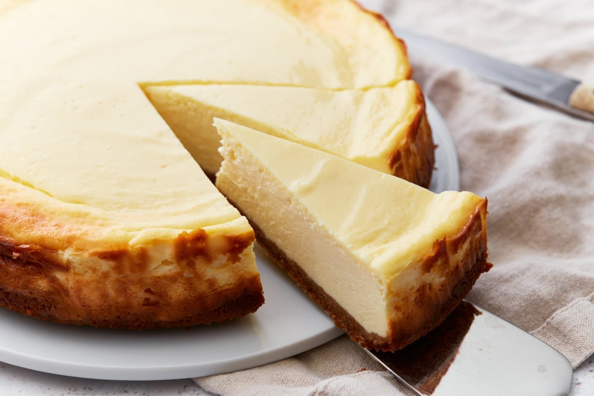 Whole gluten-free cheesecake with a slice being lifted out, showing the creamy interior and golden crust.
