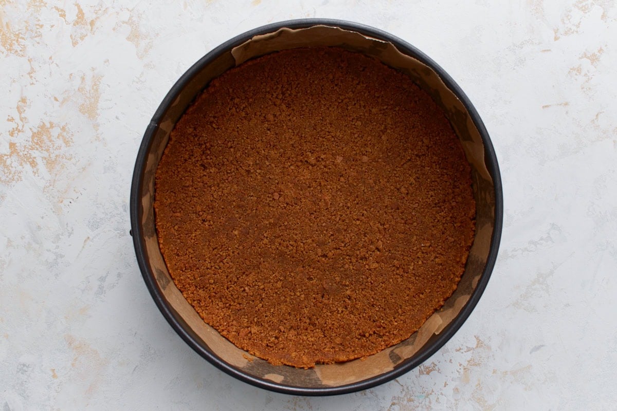 Gluten-free graham cracker crust pressed evenly into the bottom of a springform pan lined with parchment paper.