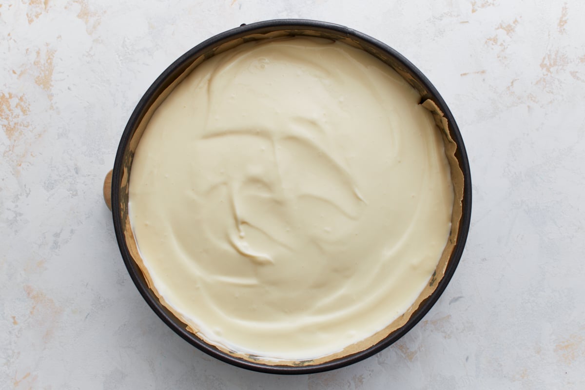 Cheesecake batter poured into springform pan, spread out evenly over the prepared crust, ready to bake.