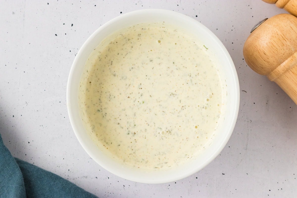 Creamy dairy-free ranch dressing fully mixed in a white bowl, flecked with herbs and spices throughout.