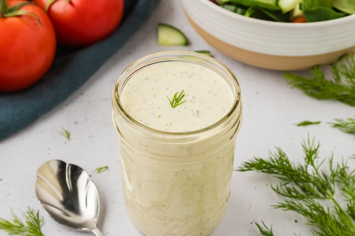 Close-up of a mason jar filled with dairy-free ranch dressing, garnished with a small sprig of fresh dill on top.