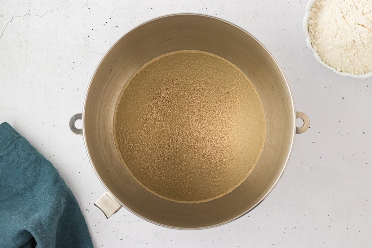 Overhead view of a mixing bowl filled with warm water and dry yeast before activation, ready for stirring.