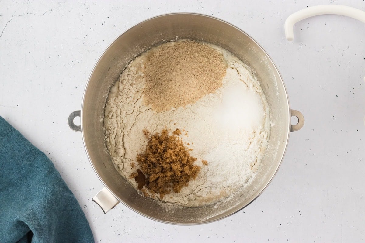 A mixing bowl with gluten-free flour, psyllium husk, brown sugar, salt, and baking powder added on top of the frothy yeast mixture.