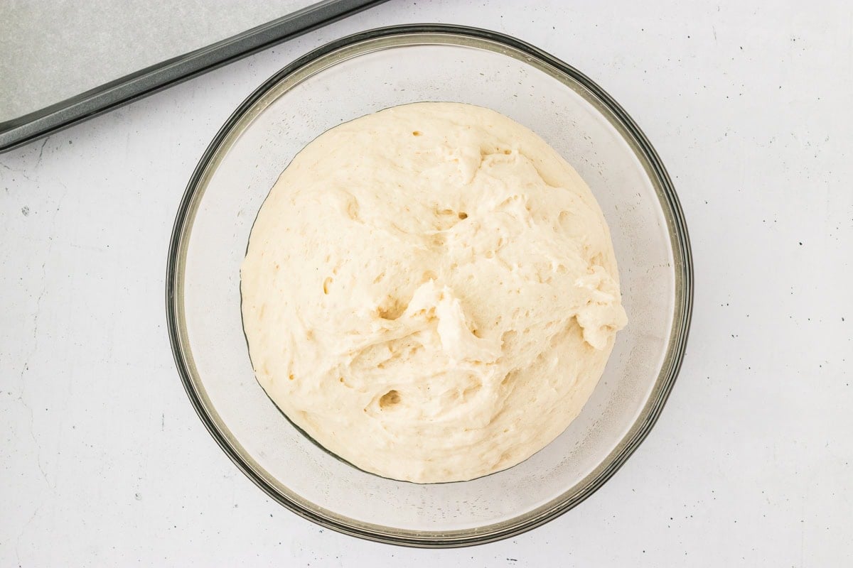 Risen gluten-free bagel dough in a glass bowl after proofing, soft and airy in texture.