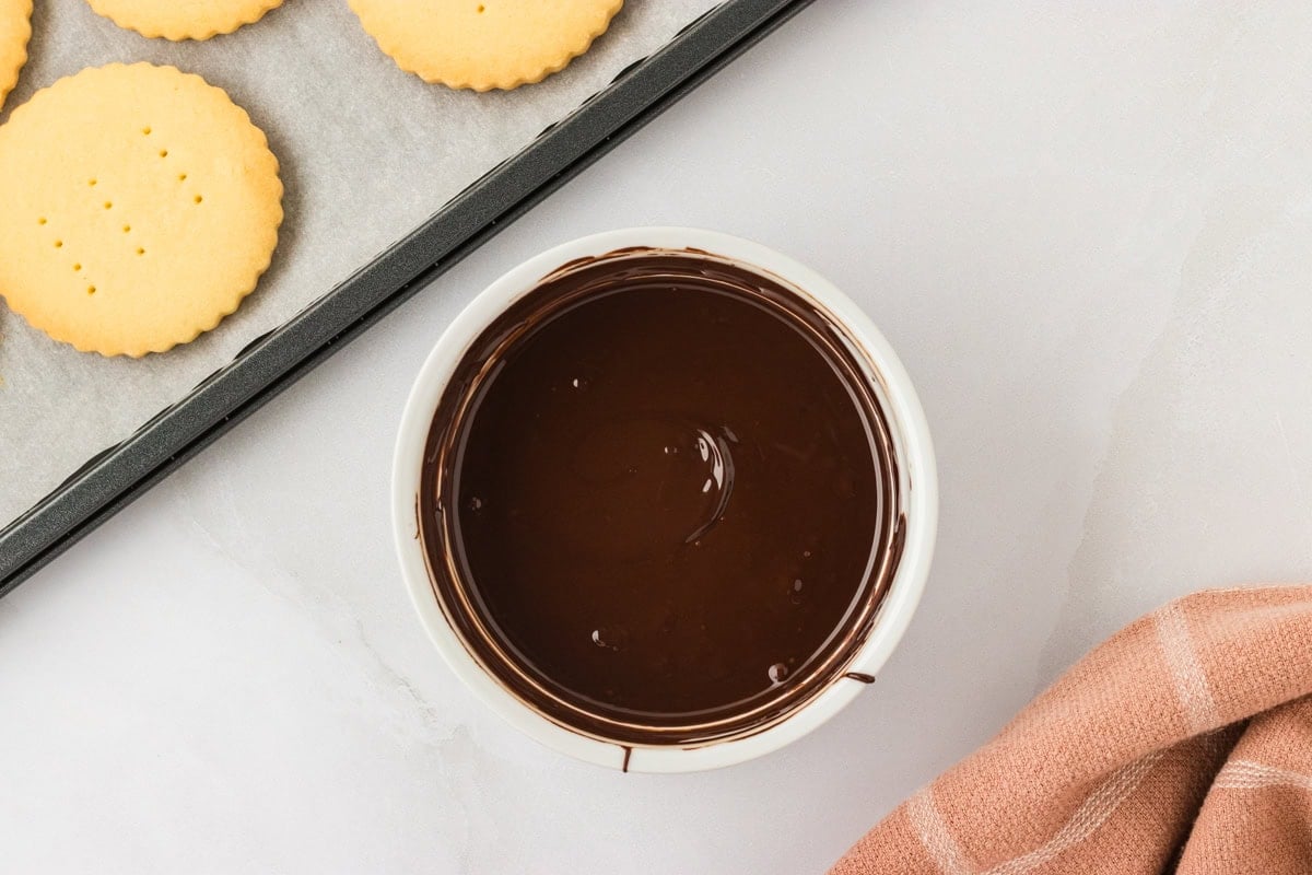 Melted chocolate in a small white bowl, ready for dipping cookies.