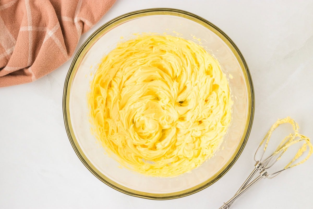 Creamed softened butter in a glass mixing bowl with a handheld electric mixer beside it.