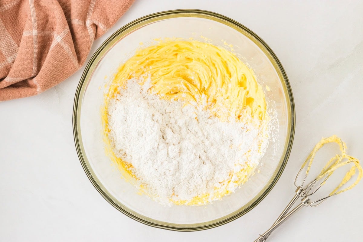 Powdered sugar added to the creamed butter in a glass bowl, ready to be mixed.