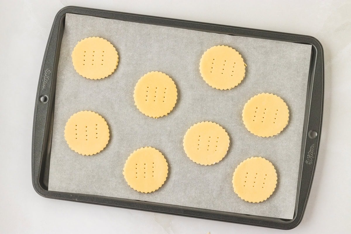 Unbaked shortbread cookies evenly spaced on a parchment-lined baking sheet, each pierced with a fork.