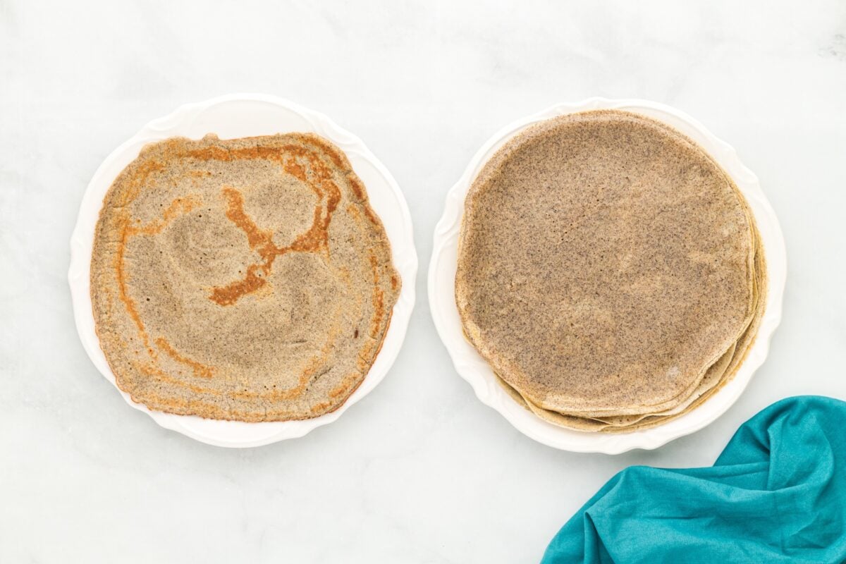 Two white plates side by side—one with a stack of evenly cooked buckwheat crepes and the other with a single crepe showing darker browned spots.