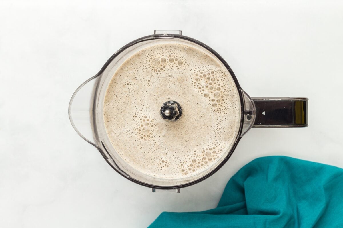A blender filled with frothy buckwheat crepe batter, resting on a white surface next to a teal napkin.