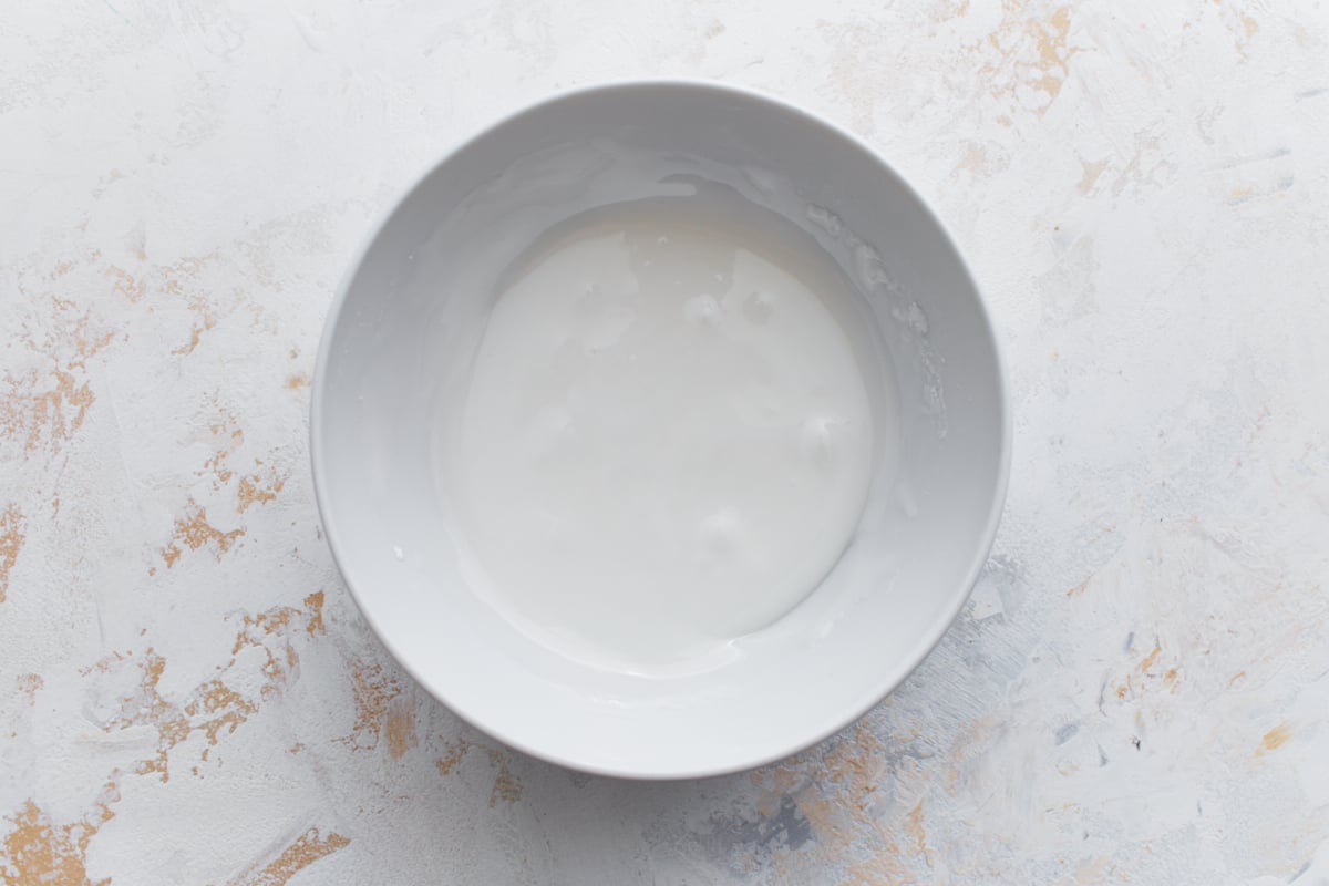 White bowl containing smooth vanilla glaze, ready to be drizzled over the muffins.