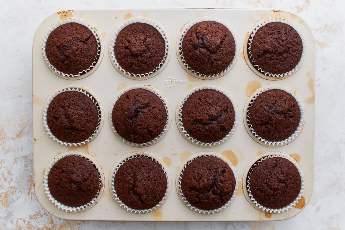 Freshly baked gluten-free chocolate cupcakes still in the muffin pan, with domed tops and a rich, dark color.
