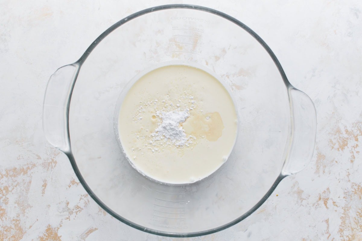 Whipped cream ingredients—heavy cream, powdered sugar, and vanilla—added to a glass mixing bowl before whipping.