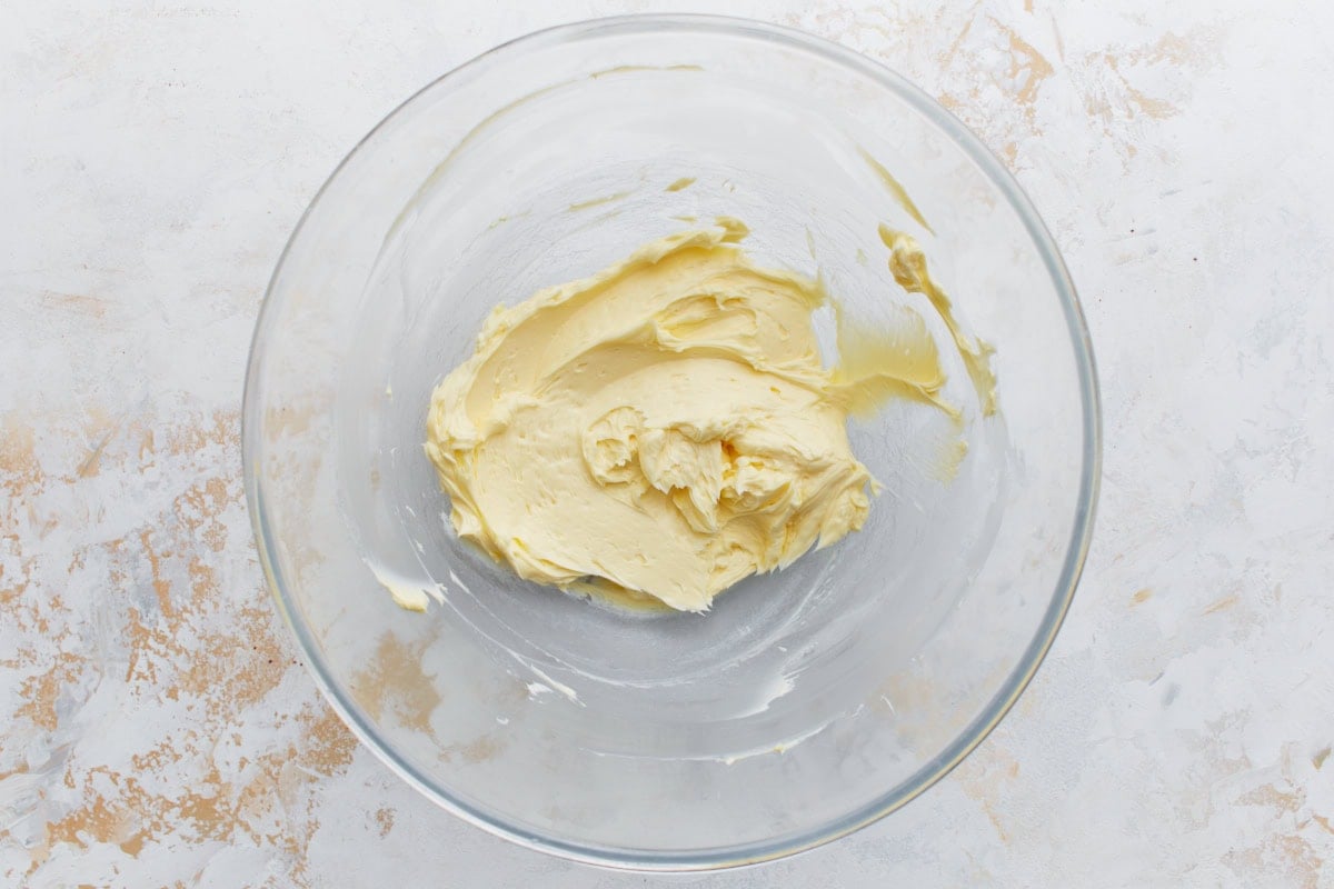 Softened butter creamed until smooth in a glass mixing bowl, ready for other frosting ingredients to be added.
