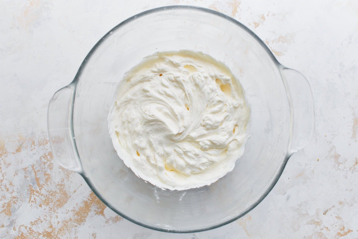 Freshly whipped cream in a glass mixing bowl with stiff peaks formed.