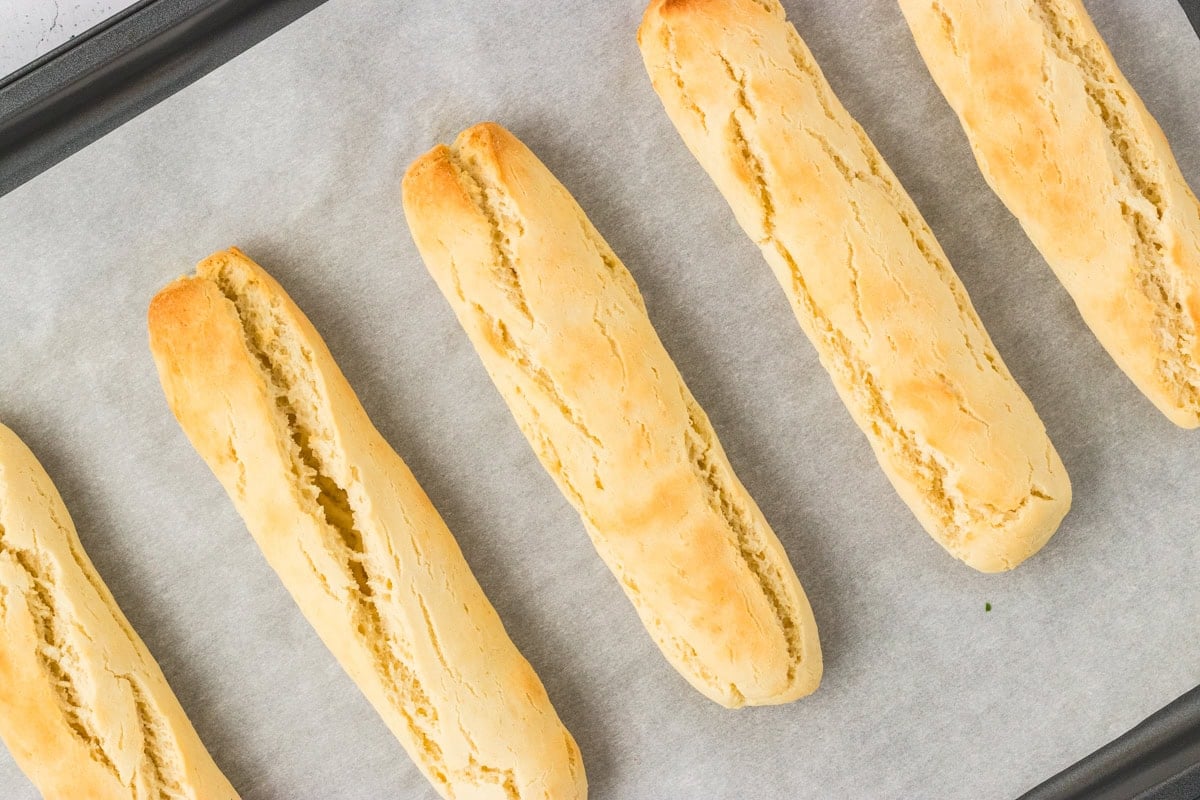 Freshly baked gluten-free breadsticks on a parchment-lined baking sheet, golden and lightly cracked on top.