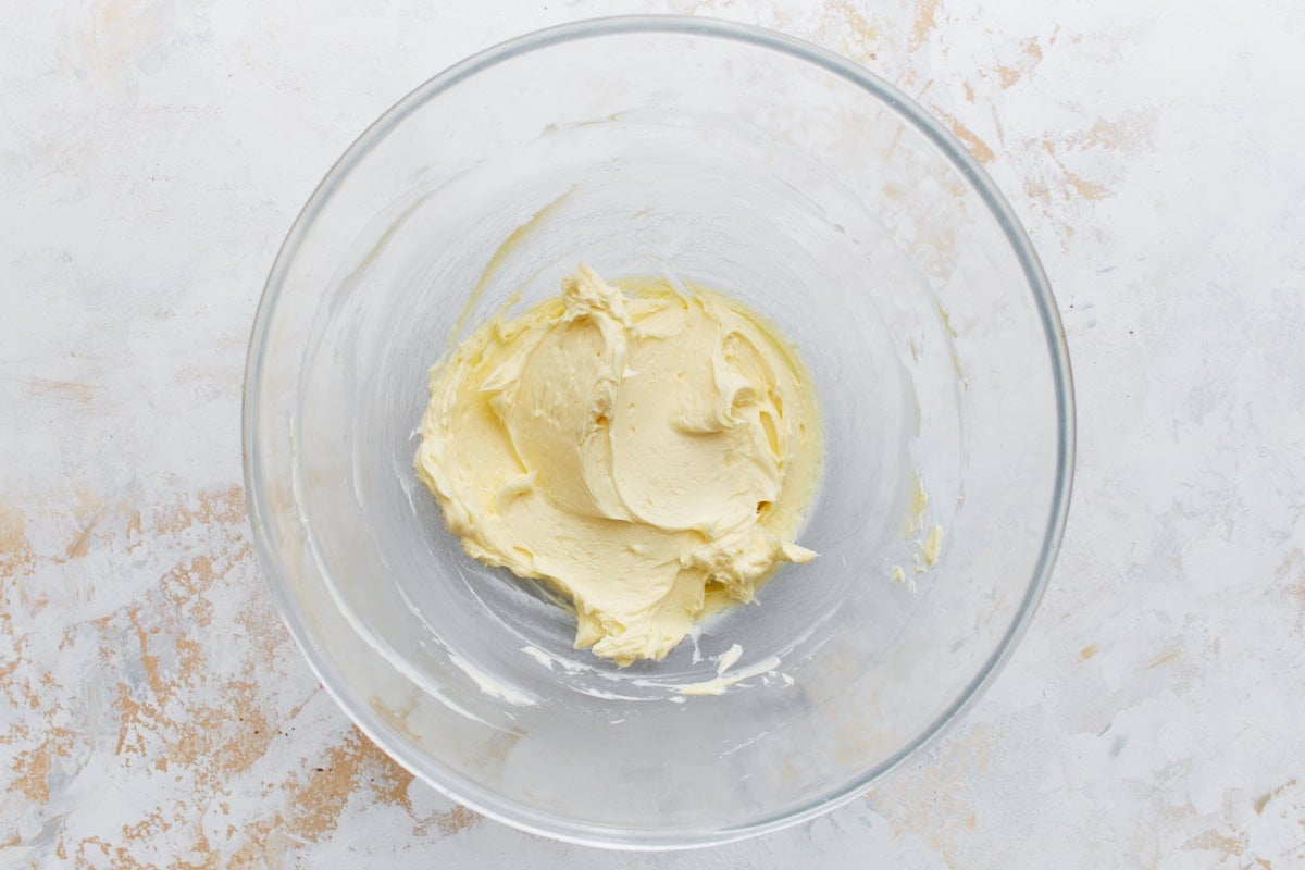 Creamy mixture of butter and extracts in a clear bowl, light and fluffy, prepped for cocoa powder and sugar.