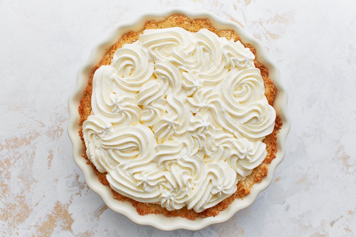 Gluten-free coconut cream pie in a pie dish, topped with piped swirls of whipped cream.