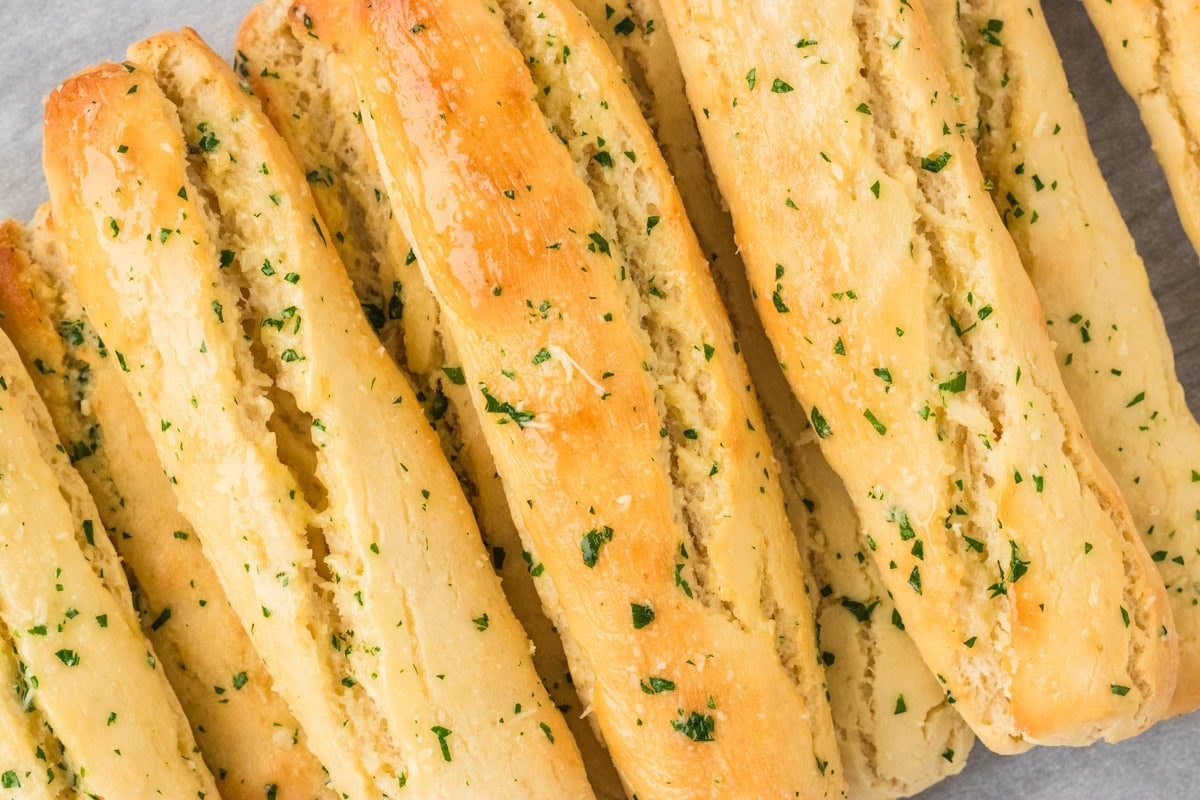 Close-up of several gluten-free breadsticks brushed with garlic butter and sprinkled with parsley.