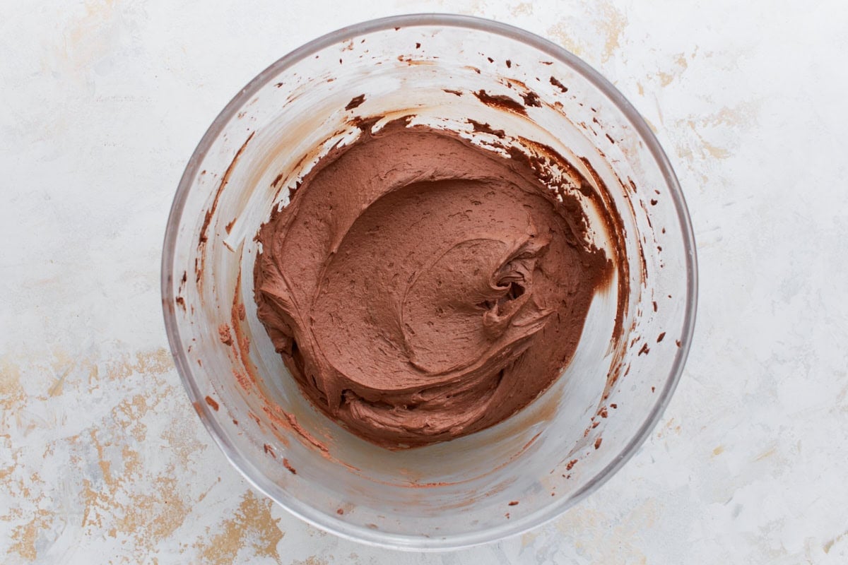 Fluffy, fully mixed chocolate buttercream frosting in a glass bowl, ready for piping onto cupcakes.