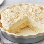 Side view of coconut cream pie with a large slice missing, showing layers of crust, custard, and whipped cream.