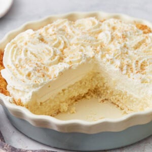 Side view of coconut cream pie with a large slice missing, showing layers of crust, custard, and whipped cream.