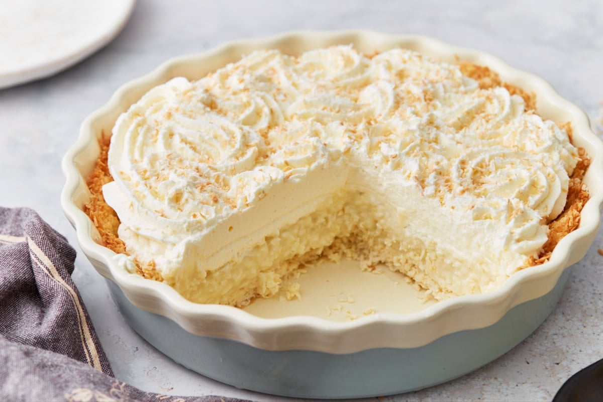 Side view of coconut cream pie with a large slice missing, showing layers of crust, custard, and whipped cream.
