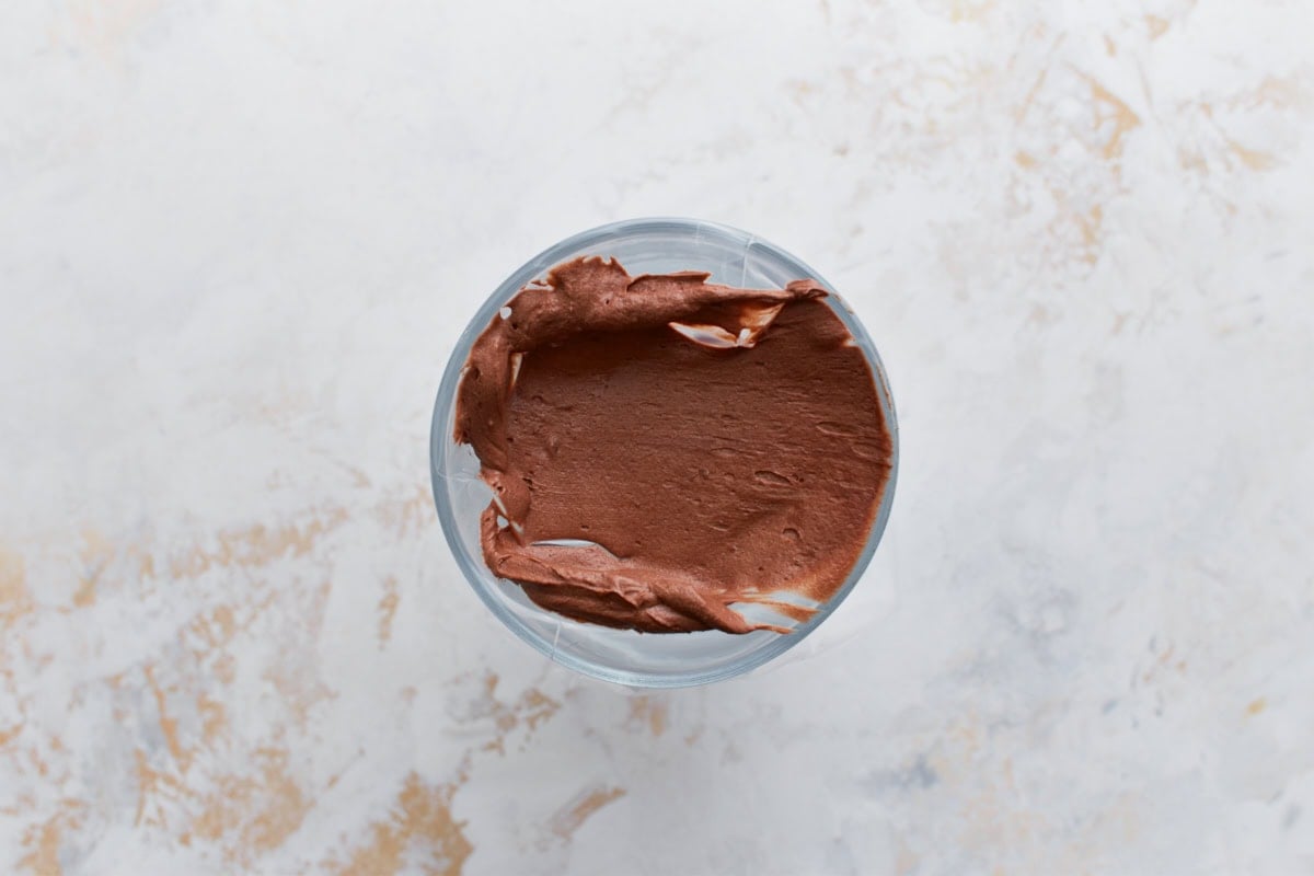 Overhead view of chocolate frosting scooped neatly into a piping bag set inside a tall cup for easy filling.