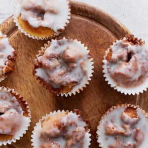 Overhead view of glazed gluten-free cinnamon roll muffins arranged on a round wooden board, showing their gooey swirls and shiny icing.