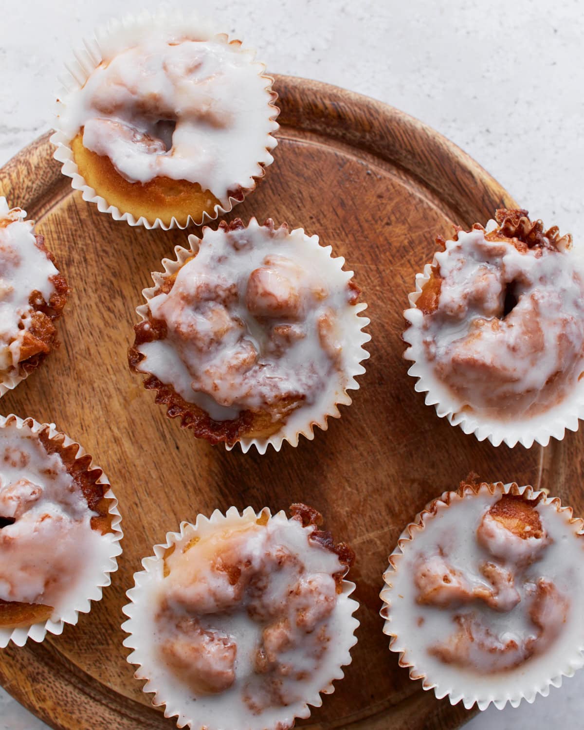 Overhead view of glazed gluten-free cinnamon roll muffins arranged on a round wooden board, showing their gooey swirls and shiny icing.