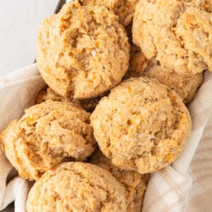 A basket filled with freshly baked gluten-free drop biscuits, nestled in a light kitchen towel.
