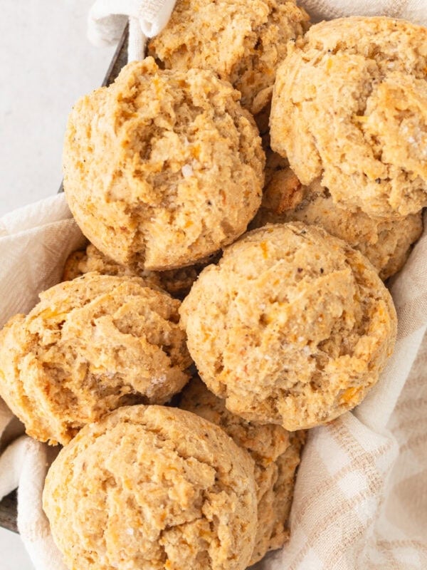 A basket filled with freshly baked gluten-free drop biscuits, nestled in a light kitchen towel.