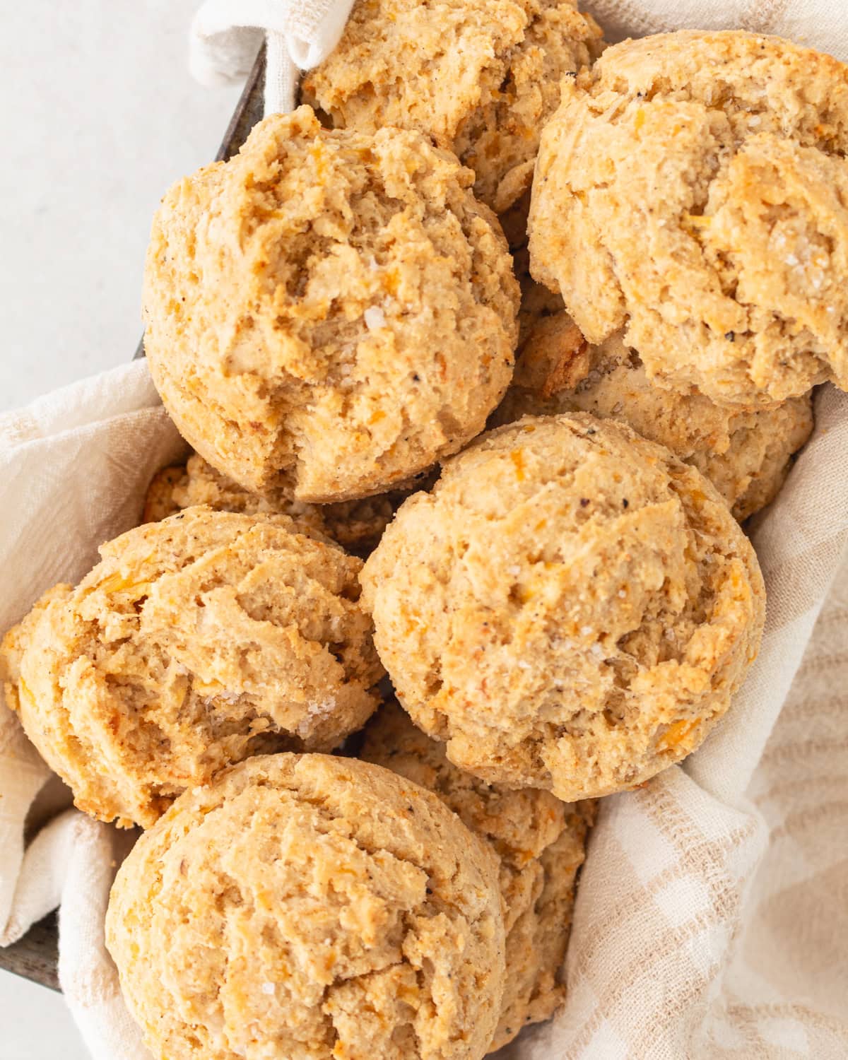 A basket filled with freshly baked gluten-free drop biscuits, nestled in a light kitchen towel.