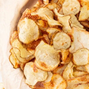 Close-up of a pile of crispy, golden-brown homemade gluten-free potato chips on parchment paper.
