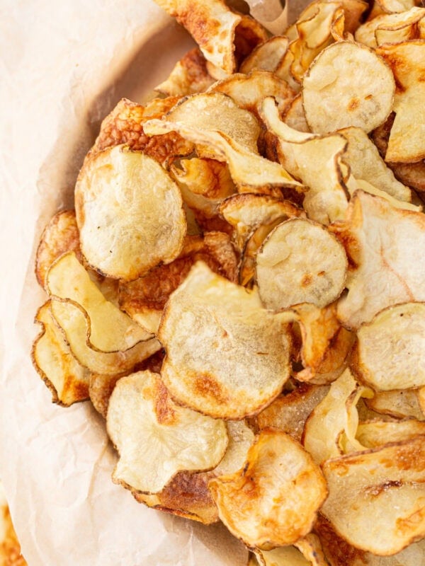 Close-up of a pile of crispy, golden-brown homemade gluten-free potato chips on parchment paper.