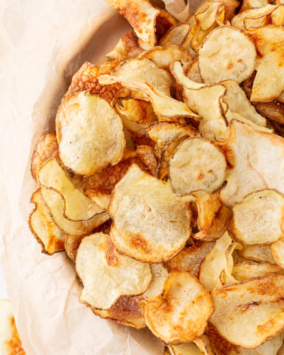 Close-up of a pile of crispy, golden-brown homemade gluten-free potato chips on parchment paper.