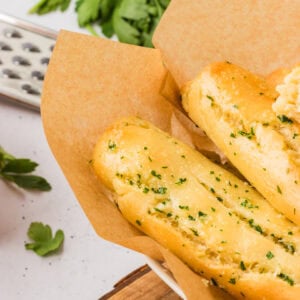 Close-up of golden gluten-free breadsticks topped with garlic and parsley, served in a parchment-lined bowl.