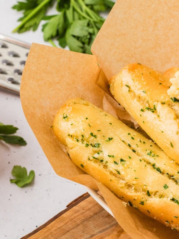 Close-up of golden gluten-free breadsticks topped with garlic and parsley, served in a parchment-lined bowl.