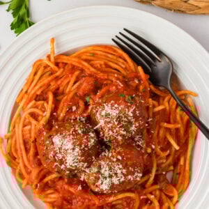Three baked gluten-free meatballs served over spaghetti with marinara sauce, topped with grated Parmesan and fresh parsley.