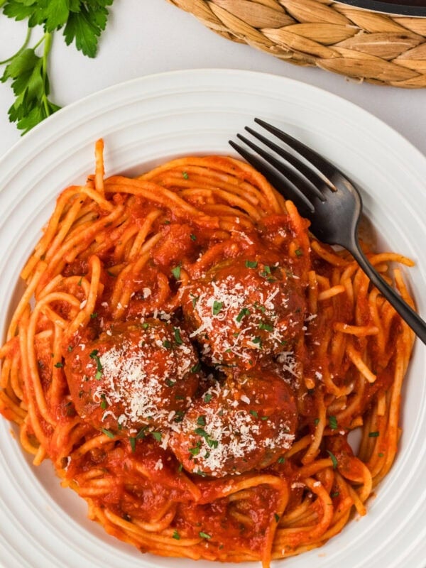 Three baked gluten-free meatballs served over spaghetti with marinara sauce, topped with grated Parmesan and fresh parsley.