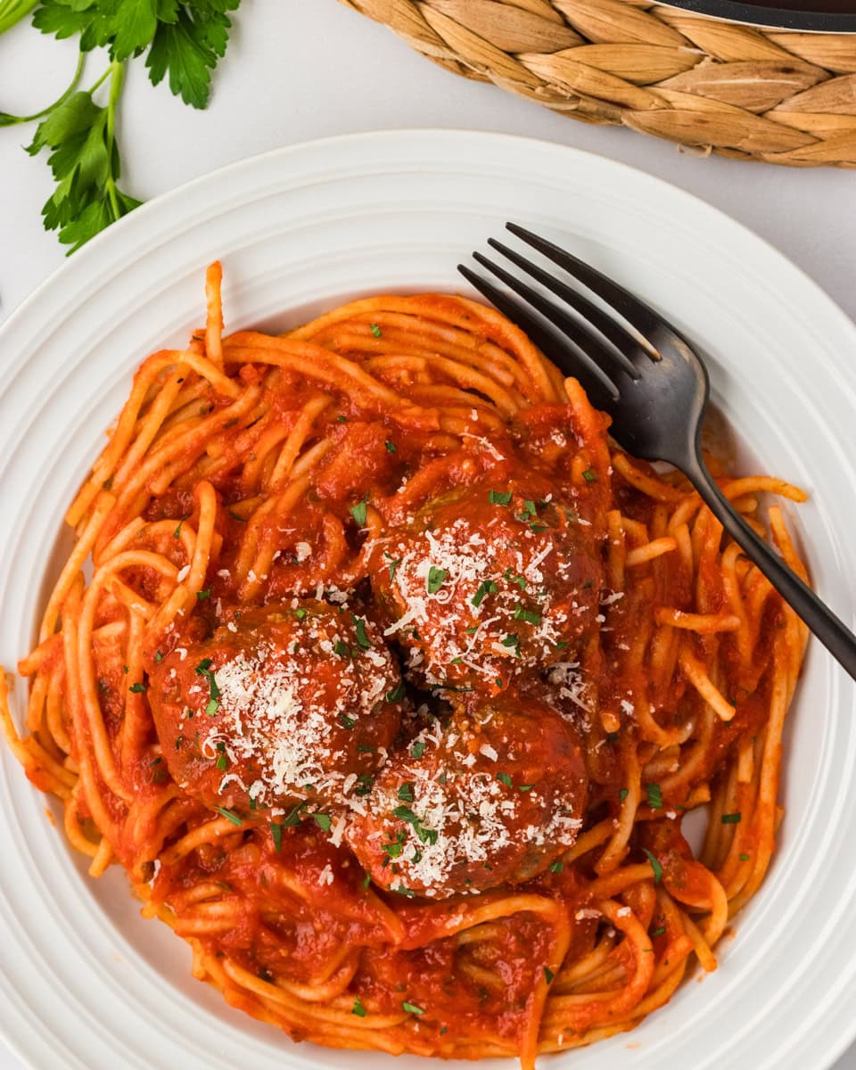 Three baked gluten-free meatballs served over spaghetti with marinara sauce, topped with grated Parmesan and fresh parsley.