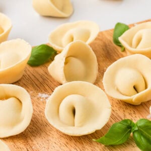 Freshly shaped gluten-free tortellini arranged on a wooden board with fresh basil leaves